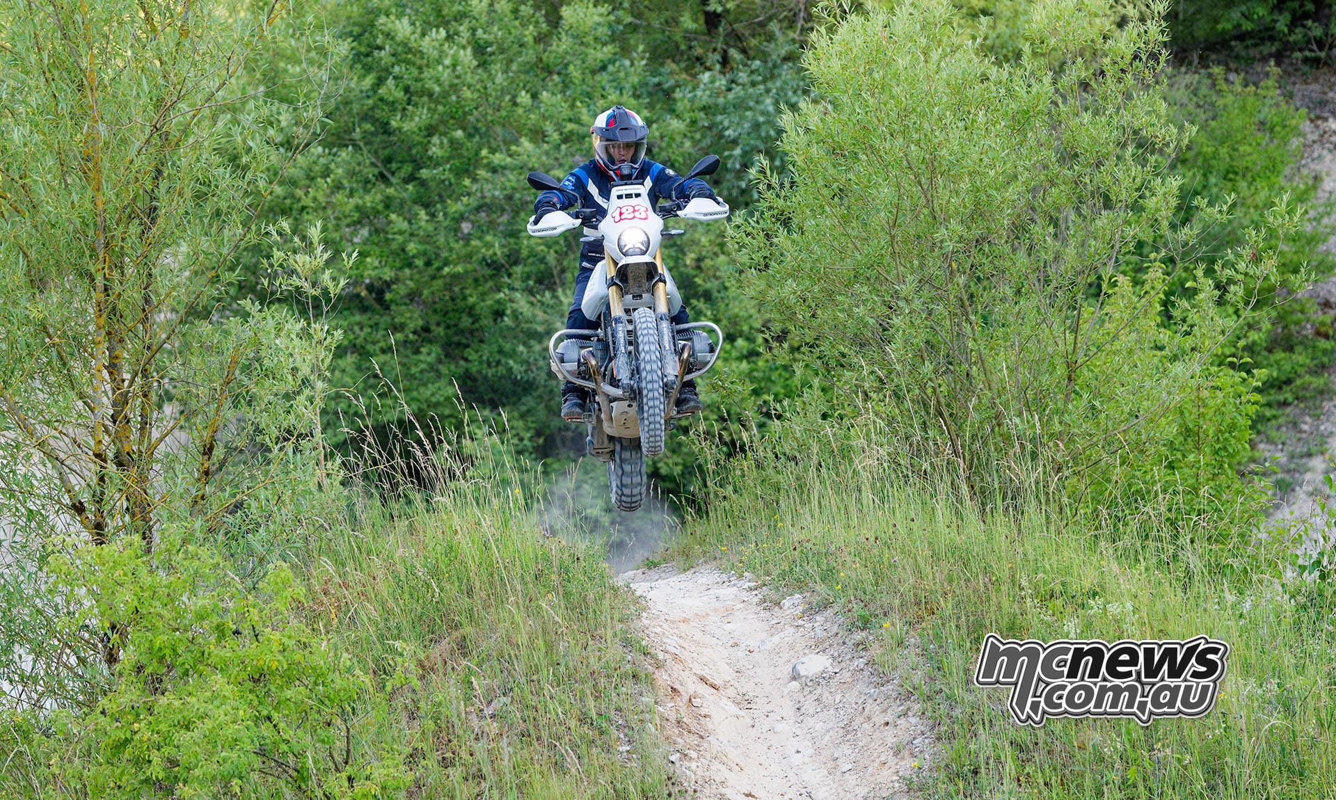 The R 12 G/S GS Trophy Competition Bike airborne over a rise on a narrow off-road trail